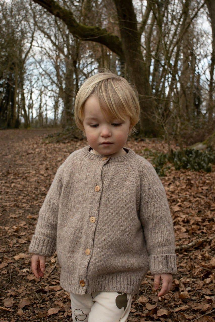 Child wearing a hand-knit Arega cardigan in a forest